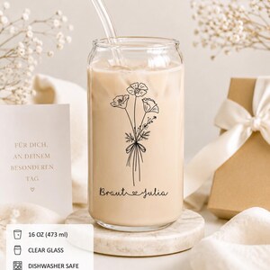Könnte beinhalten: Ein 473 ml klares Glas in Dosenform mit Glasstrohhalm, gefüllt mit einem beigen Getränk. Das Glas zeigt eine schwarze Strichzeichnung eines Blumenstraußes und den Text Braut Julia mit einem Herzsymbol zwischen den beiden Wörtern.