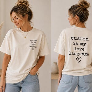Könnte beinhalten: Ein cremefarbenes Kurzarm-T-Shirt mit schwarzem Text auf der linken Brustseite, der "custom is my love language" lautet, ergänzt durch ein kleines Herz. Auf der Rückseite ist derselbe Text mit Herz in einer größeren, zentrierten Form.