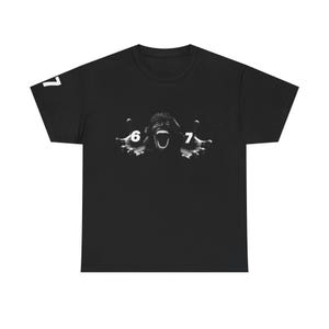 May include: Black t-shirt featuring a black and white graphic of a screaming face with outstretched hands. The numbers "6" and "7" are on the hands, and the number "7" is on the left sleeve.