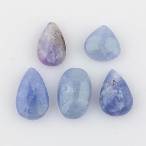 May include: Five polished gemstones arranged in a group. One stone is a teardrop-shaped lavender and grey piece, while the other four are smooth, rounded stones in varying shades of light blue, including three teardrop shapes and one oval.