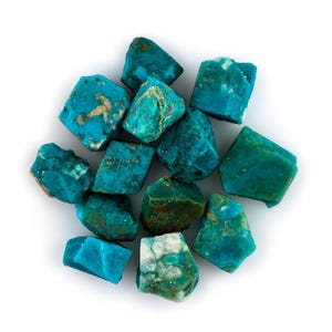 May include: A collection of raw turquoise stones, each with a unique shape and texture. The stones display a vibrant turquoise color with hints of brown and white, creating a natural and earthy aesthetic. The stones are arranged on a white background.