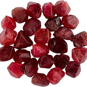 Peut inclure: Une collection de cristaux de pierres précieuses rouges brutes et détachées aux formes irrégulières et facettées. Les pierres présentent des nuances variées de cramoisi profond et de rouge rubis translucide, avec des textures naturelles.