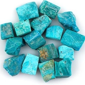 Puede incluir: Colección de piedras preciosas de amazonita en bruto de color turquesa. Las piedras varían en tamaño y forma, con una mezcla de superficies lisas y texturizadas. Algunas piedras tienen toques de verde y marrón.