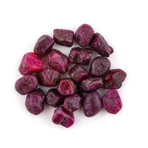 Puede incluir: Un conjunto de piedras preciosas de rubí en bruto, que muestran una gama de tonos rojos oscuros y violáceos. Las piedras sin pulir, de tamaños y formas variadas, tienen una textura natural y orgánica. Las piedras están dispuestas sobre un fondo blanco.