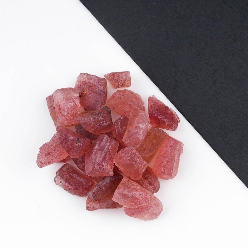 Puede incluir: Una colecci&oacute;n de peque&ntilde;os fragmentos de piedras preciosas en bruto y sin pulir en varios tonos de rosa transl&uacute;cido y rojo intenso. Estas piezas minerales irregulares y angulares presentan una textura cristalina rugosa.