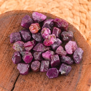 Peut inclure: Un ensemble de pierres précieuses de rubis brutes, de différentes nuances de rouge et de violet. Les pierres non taillées sont présentées sur une surface en bois rustique, mettant en valeur leurs textures et couleurs naturelles.