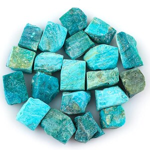 Puede incluir: Una colección de piedras de amazonita en bruto en tonos turquesa y verde azulado. Las piedras tienen un aspecto natural y texturizado, con variaciones de color y forma. La disposición es circular, con las piedras muy juntas.