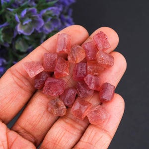 Puede incluir: Una colección de pequeñas piedras preciosas rojas, crudas y translúcidas, con formas irregulares y angulares y superficies facetadas. Estas piedras muestran diversos tonos de rosa intenso y carmesí, exhibiendo una textura natural y sin pulir con inclusiones visibles.