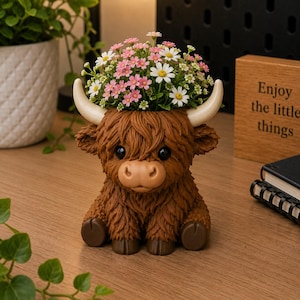 May include: A brown Highland cow planter with a fluffy texture, large black eyes, and white horns. The planter is filled with a mix of pink and white flowers. A wooden sign with the text "Enjoy the little things" is in the background.