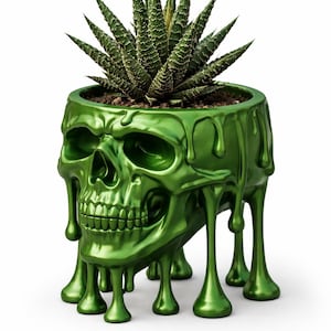 Puede incluir: Una maceta verde con forma de calavera con una planta suculenta. La maceta tiene un acabado brillante y un diseño de goteo. La planta tiene hojas verdes y puntiagudas. Un artículo decorativo único.