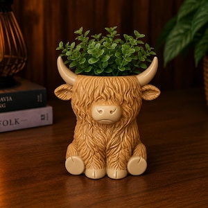 May include: A tan-colored Highland cow planter with a green plant inside. The planter has a detailed design, including horns, ears, and a shaggy coat. The planter is sitting on a wooden surface.