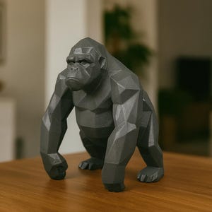 May include: A gray, geometric gorilla sculpture. The ape is in a quadrupedal stance, with a detailed, angular design. The sculpture is placed on a wooden surface, with a blurred background.