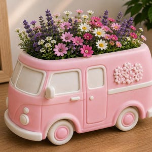 May include: A light pink ceramic planter shaped like a vintage van, featuring white trim and a raised floral relief on the side. The planter is filled with a vibrant arrangement of purple lavender, pink daisies, and small white flowers.