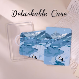 May include: A light blue detachable phone case with a winter landscape design featuring mountains, ice floes, and penguins. The clear case is visible next to the phone case. The text "Detachable Case" is at the top.