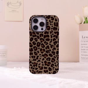 May include: A smartphone case featuring a brown and black leopard print pattern. The case has a rectangular shape with rounded corners and a cutout for the camera lens array on the upper left side, showing the device's three circular lenses.