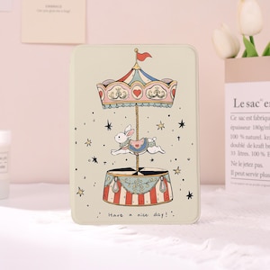 May include: A rectangular tin with a carousel design. The carousel features a white rabbit, a red flag, and the text "Have a nice day!". The tin has a cream-colored background with star accents and a decorative border.