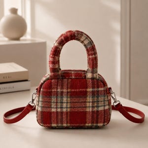 Peut inclure: Un petit sac à main avec un motif à carreaux rouge, blanc et gris. Le sac présente un haut arrondi, deux anses courtes rembourrées et une bandoulière rouge amovible fixée par des attaches en métal argenté. Le compartiment se ferme par zip.