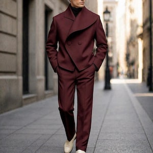 May include: A burgundy suit with a unique asymmetrical lapel design. The double-breasted jacket and matching trousers are paired with a black turtleneck and white loafers. The suit is a stylish ensemble for formal occasions.