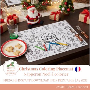 May include: A white Christmas coloring placemat with various holiday-themed illustrations, including a snow globe, gingerbread men, and ornaments. The placemat is accompanied by colored pencils, a plate of cookies, and a Santa Claus figurine. The text "JOYEUX NOËL" is visible.