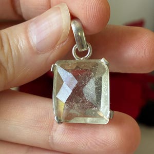 May include: A rectangular, faceted, pale yellow gemstone pendant set in a silver-toned metal prong setting. The stone features a clear, multi-faceted surface that reflects light, and the pendant includes a small silver-toned metal bail at the top.