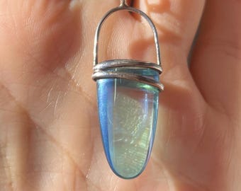 May include: A silver pendant necklace featuring a blue and iridescent crystal. The crystal is encased in a silver wire wrap and suspended from a delicate silver chain. The pendant has a unique, elongated shape.