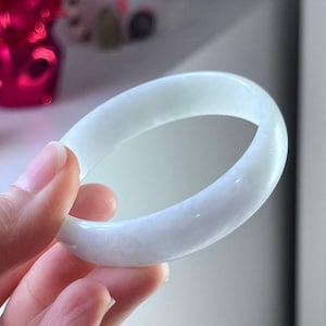 Può includere: Un braccialetto bangle di giada verde pallido. Il braccialetto ha una forma ovale solida e sembra essere fatto di una pietra traslucida. La giada ha una sottile variazione di colore naturale. Questo pezzo è un tipo di gioiello.