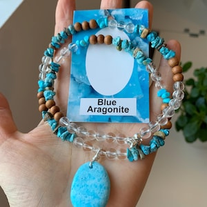 Könnte beinhalten: Ein Set aus blauer Aragonit-Halskette und Armband. Die Halskette besteht aus klaren Perlen, Türkis-Chips und Holzperlen. Das Armband hat ein ähnliches Design. Ein blauer Aragonit-Anhänger hängt an der Halskette. Der Text "Blue Aragonite" steht auf einer blauen Karte.