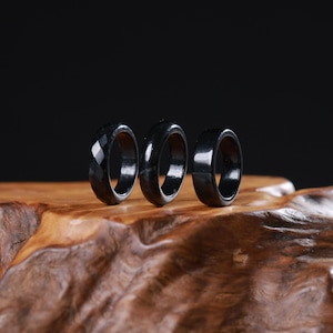 May include: Three black rings arranged in a row. The first ring on the left features a faceted geometric surface, while the middle and right rings have smooth, polished surfaces. Each ring has a circular band design with a hollow center.