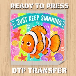 May include: A square DTF transfer sheet featuring a bright orange clownfish with white stripes, surrounded by red starfish and colorful seashells. The text "JUST KEEP SWIMMING" is printed on a teal banner above the fish with a small heart icon.
