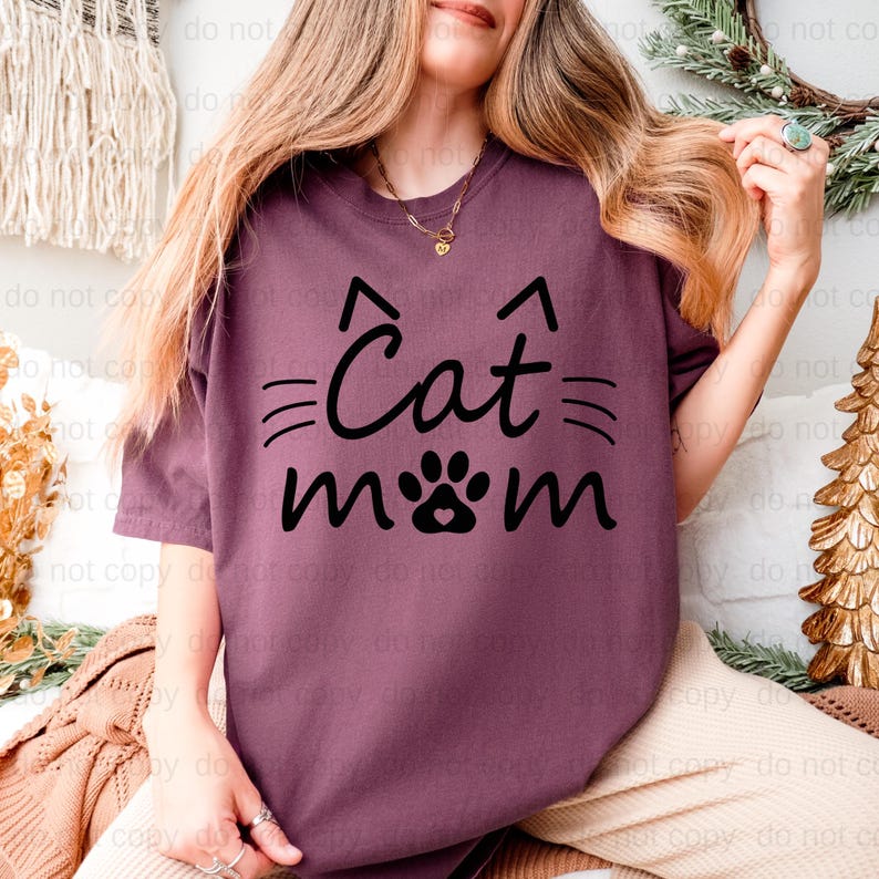 A woman wearing a purple t-shirt with the text "Cat mom" printed on it, smiling and holding her hair.