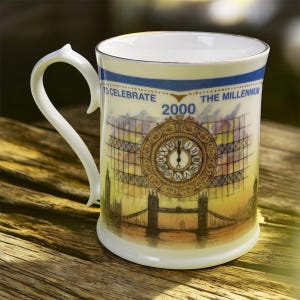 Puede incluir: Taza de cerámica blanca con un diseño de asa único. La taza presenta una colorida ilustración de una torre del reloj y un puente, con el texto "TO CELEBRATE THE MILLENNIUM 2000". El borde y el asa están adornados con oro.