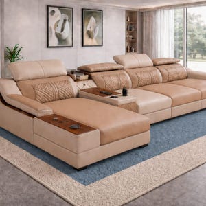 以下が含まれることがあります： モダンなリビングルームにある大きなコーナーソファ。ソファは、模様入りのアクセントと内蔵のサイドテーブルを備えた、明るいタン色の革張りが特徴です。青とベージュのラグの上にあり、ニュートラルなトーンの壁と大きな窓があります。