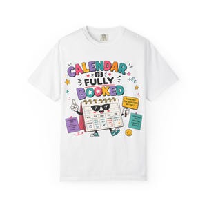 Puede incluir: Una camiseta blanca con un gráfico colorido de un personaje calendario con gafas de sol. El texto dice CALENDAR IS FULLY BOOKED, con notas adicionales que dicen THANK YOU FOR RESPECTING MY TIME y otros pequeños bloques de texto alrededor.