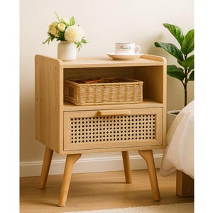 May include: A light-colored wooden nightstand with a drawer and a shelf. The drawer has a woven rattan front. A woven basket sits on the shelf, and a small white vase with flowers and a teacup are on top.
