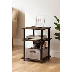 May include: A dark brown, three-tiered side table with black supports. The top shelf holds a framed picture, the middle shelf has books, and the bottom shelf contains a gray fabric bin. The table is 24 inches tall.