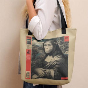 May include: Beige tote bag with a Mona Lisa-style chimpanzee portrait. The image is set against a landscape backdrop. The bag has black handles and a red vertical stripe with text on the left side.