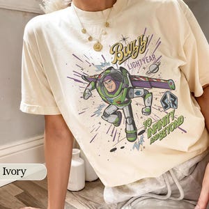 Puede incluir: Camiseta de color marfil con un gr&aacute;fico de Buzz Lightyear, el texto "Buzz Lightyear" y "To Infinity and Beyond". El dise&ntilde;o incluye un tema espacial con un planeta y un cohete. La camiseta es de corte holgado.