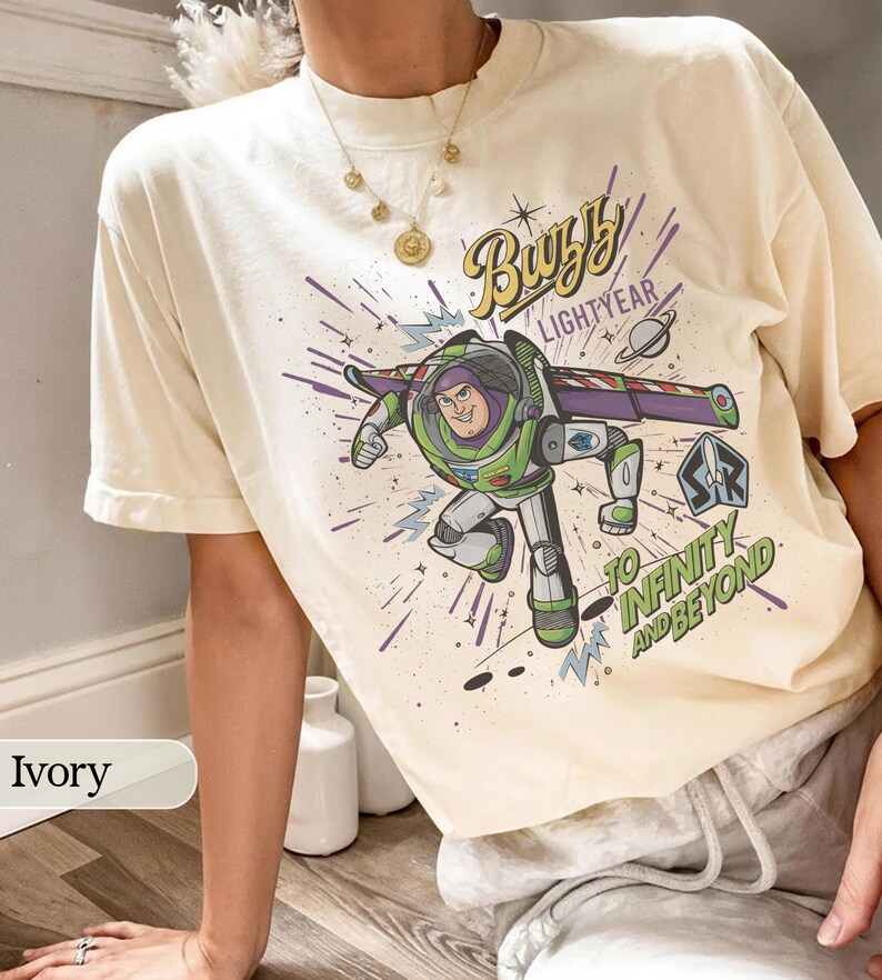 Puede incluir: Camiseta de color marfil con un gr&aacute;fico de Buzz Lightyear, el texto "Buzz Lightyear" y "To Infinity and Beyond". El dise&ntilde;o incluye un tema espacial con un planeta y un cohete. La camiseta es de corte holgado.