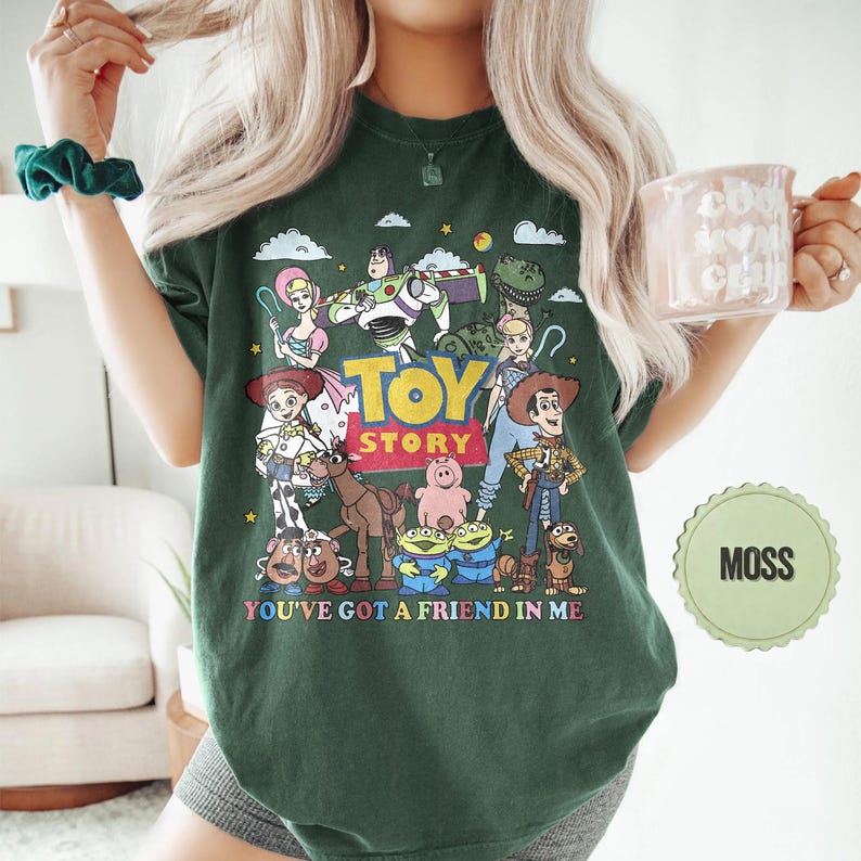 May include: A dark green t-shirt featuring a colorful graphic of characters from the animated film "Toy Story." The design includes the words "Toy Story" and "You've Got a Friend in Me."