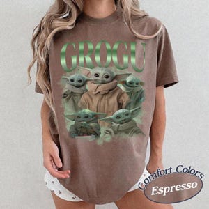 Op de afbeelding: Espresso-kleurig T-shirt met het woord "GROGU" in groen, met meerdere Grogu-personages. Het shirt is van het merk Comfort Colors.