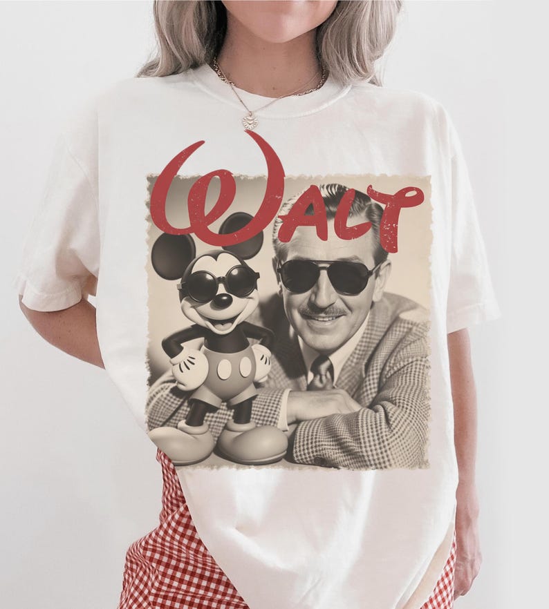 May include: White t-shirt featuring a sepia-toned image of Walt Disney and Mickey Mouse wearing sunglasses. The word "Walt" is written in red script above the image. The shirt is a casual, unisex style.