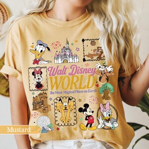 May include: Mustard-colored t-shirt featuring various Disney characters and the text "Walt Disney World". The design includes Donald Duck, Minnie Mouse, Mickey Mouse, and other characters, along with a castle and fireworks.