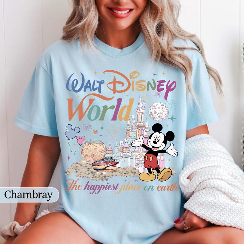 May include: Light blue t-shirt with a colorful "Walt Disney World" graphic featuring Mickey Mouse, a castle, and the phrase "The happiest place on earth." The design includes balloons and fireworks.