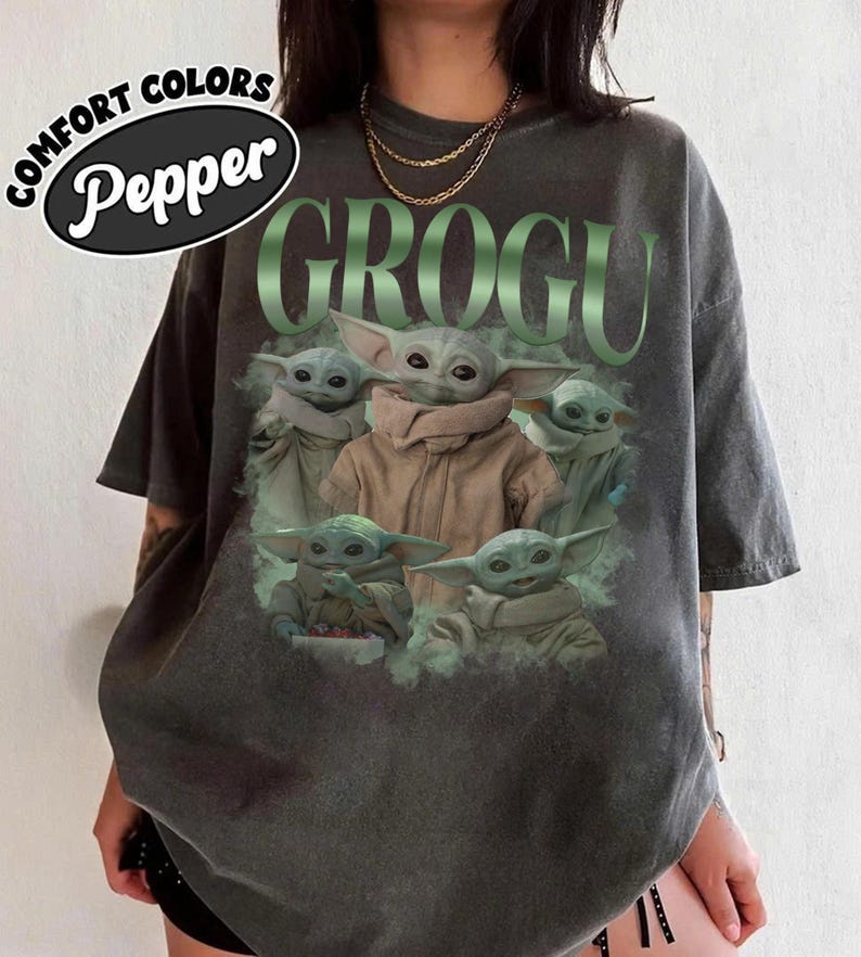 Op de afbeelding: Donkergrijs T-shirt met een afbeelding van Grogu uit The Mandalorian. Het woord "GROGU" is in het groen boven de afbeelding van Grogu gedrukt. Het shirt heeft ook de woorden "COMFORT COLORS" en "Pepper" erop staan.