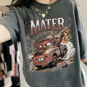 May include: Dark gray t-shirt featuring a graphic of Mater from the movie Cars. The design includes the word "MATER" in large, distressed lettering above an illustration of the character Mater, a tow truck, with lightning bolts and tools.
