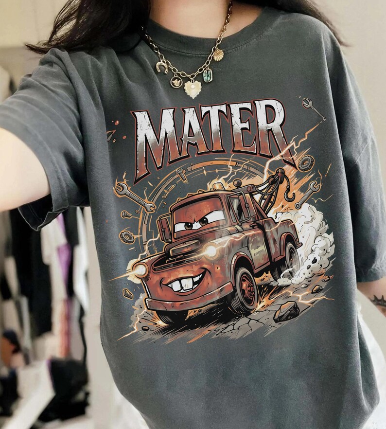 May include: Dark gray t-shirt featuring a graphic of Mater from the movie Cars. The design includes the word "MATER" in large, distressed lettering above an illustration of the character Mater, a tow truck, with lightning bolts and tools.