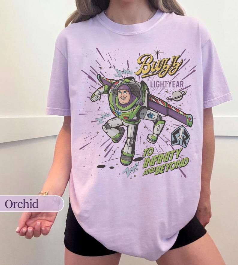 Puede incluir: Camiseta color orqu&iacute;dea con un gr&aacute;fico de Buzz Lightyear en una pose din&aacute;mica. El dise&ntilde;o incluye el texto "Buzz Lightyear" y "To Infinity and Beyond" con elementos espaciales. La camiseta es de uso casual y c&oacute;modo.