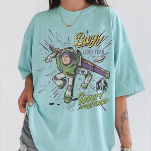 Puede incluir: Camiseta azul claro con un dise&ntilde;o de Buzz Lightyear. El dise&ntilde;o incluye el texto "Buzz Lightyear" y "To Infinity and Beyond" con un fondo espacial. La camiseta tiene un corte holgado y oversize.