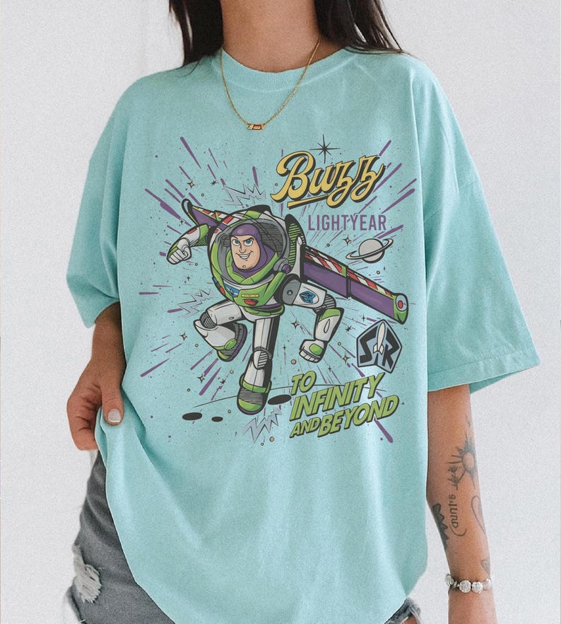 Puede incluir: Camiseta azul claro con un dise&ntilde;o de Buzz Lightyear. El dise&ntilde;o incluye el texto "Buzz Lightyear" y "To Infinity and Beyond" con un fondo espacial. La camiseta tiene un corte holgado y oversize.