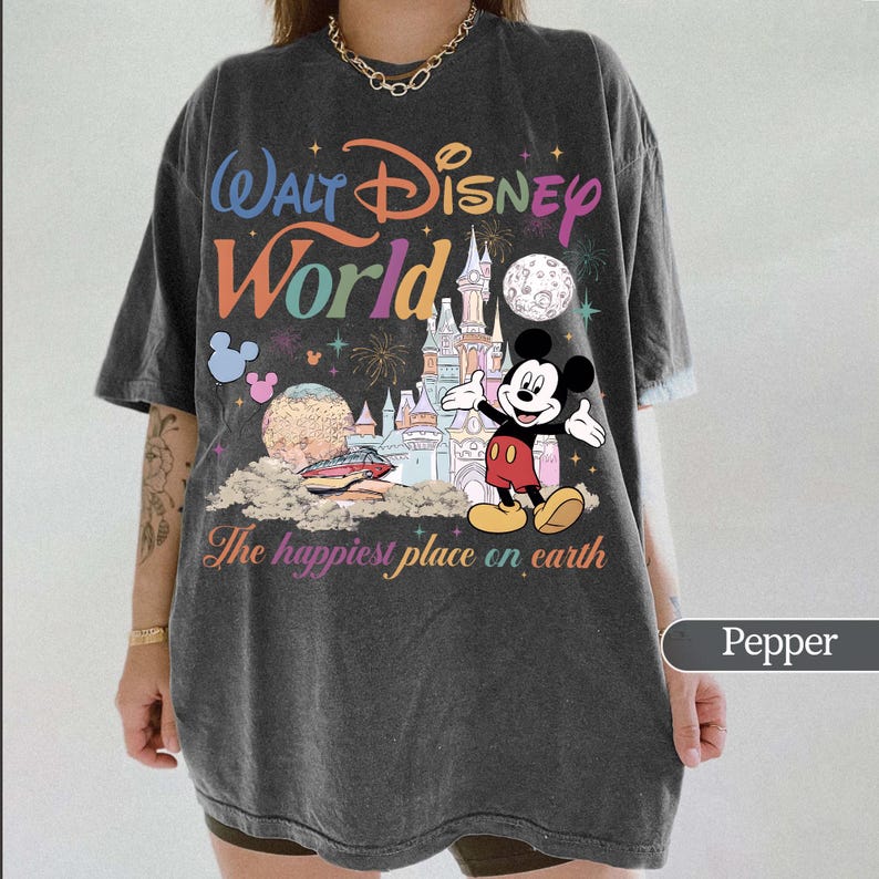 May include: Pepper-colored t-shirt featuring a colorful Walt Disney World graphic. The design includes the park's logo, a castle, Mickey Mouse, and the phrase "The happiest place on earth."